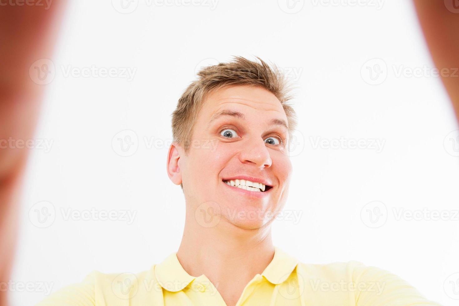 Comic mad man in casual t shirt smiling on camera with thumb up while taking selfie isolated over white background photo