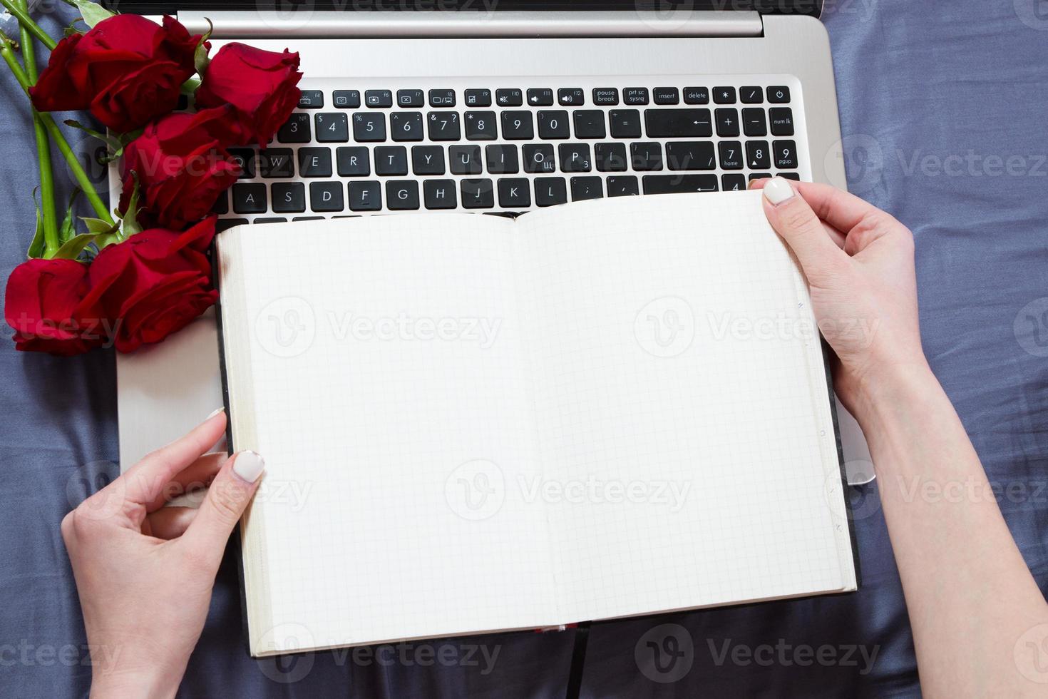Close up - Hands holding an open notebook top view mock up. Topview on laptop keyboard and bouquet of flowers background photo