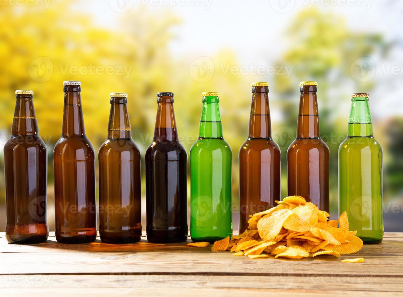 beer bottles and potato chips on wooden table on blurred park background photo