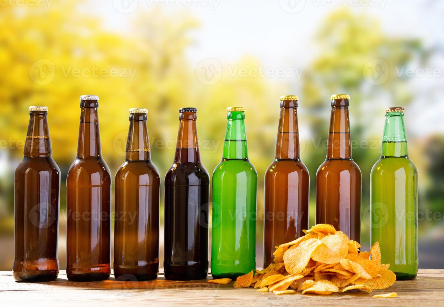 beer bottles and potato chips on wooden table on blurred park background photo