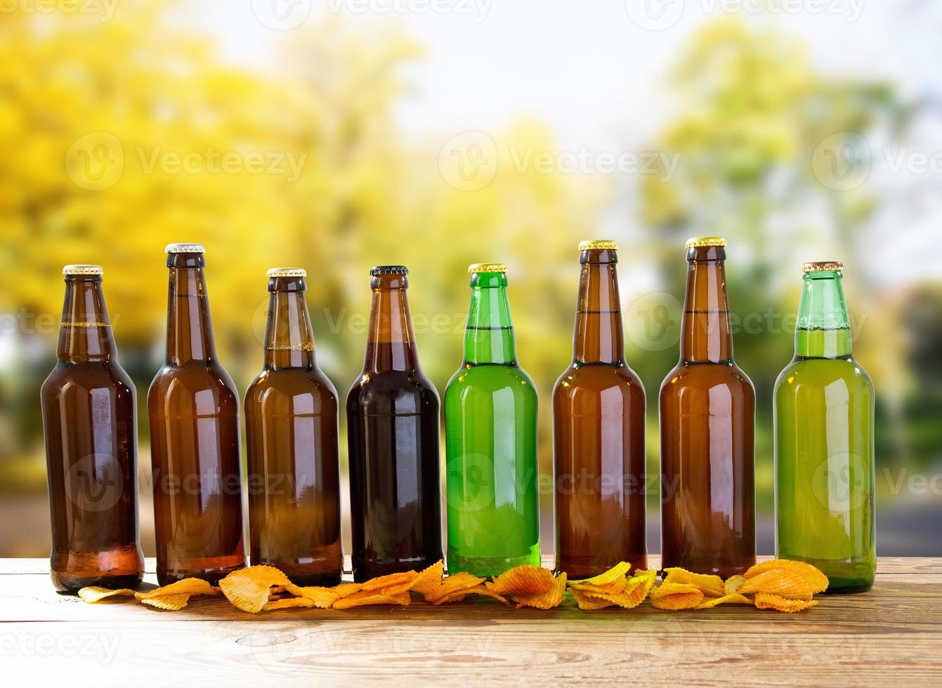 beer bottles and potato chips on wooden table on blurred park background photo