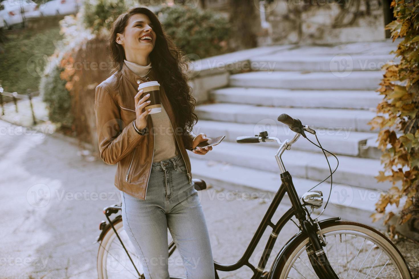 Young woman with mobile phone drink coffee to go by the bicycle on autumn day photo