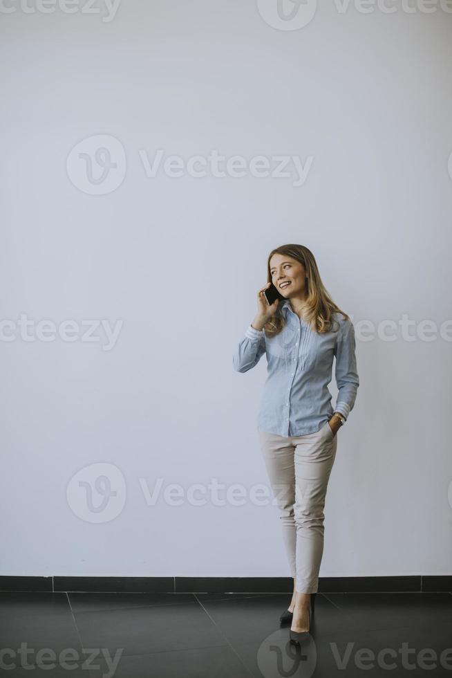 mujer de negocios, utilizar, teléfono móvil, por la pared, en, la oficina foto