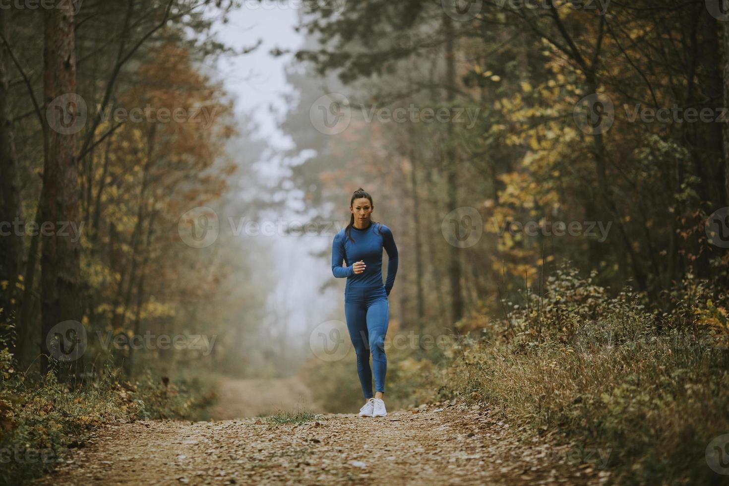 Mujer joven corriendo hacia la cámara en la pista forestal en otoño foto