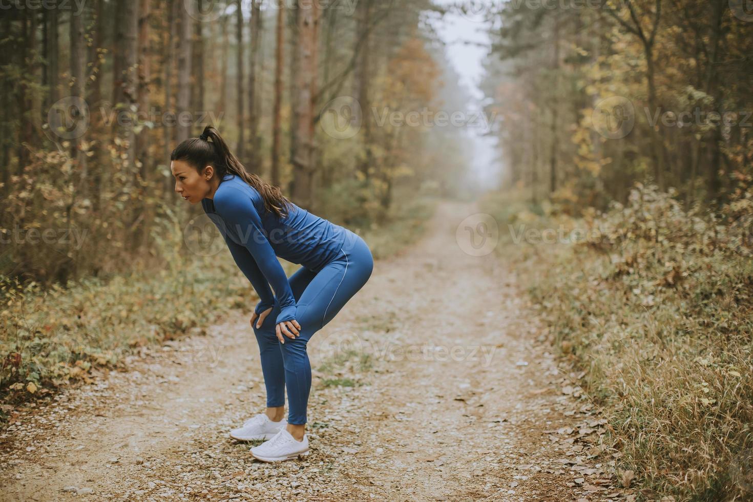 Mujer joven tomar un descanso durante el ejercicio al aire libre en la pista forestal en otoño foto