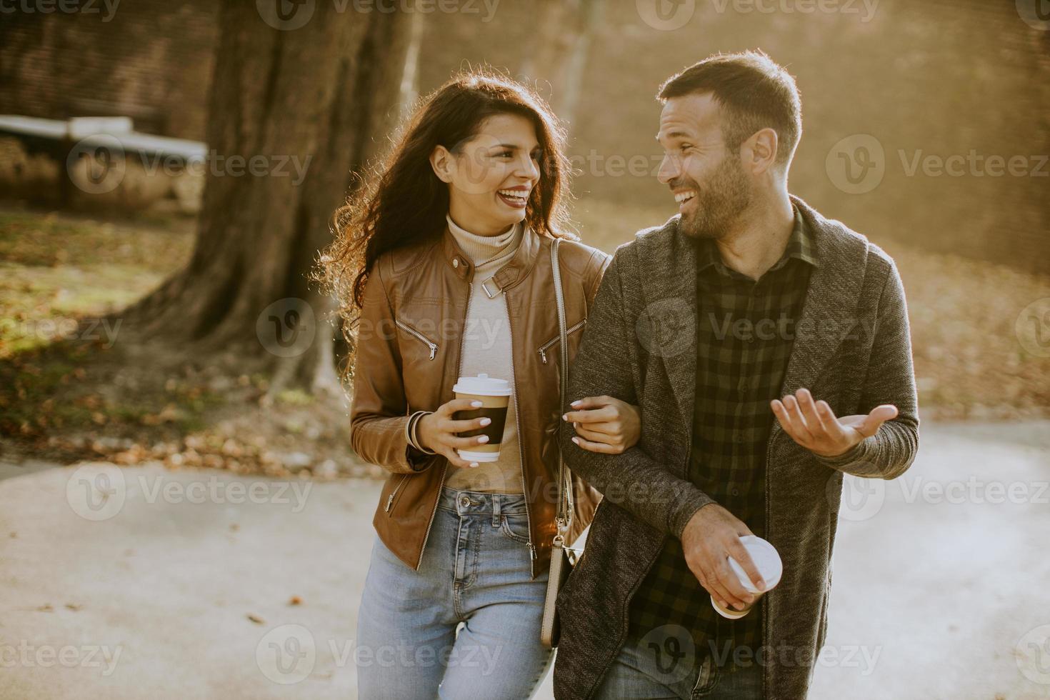 Pareja joven caminando en el parque de otoño con café para llevar tazas en las manos foto