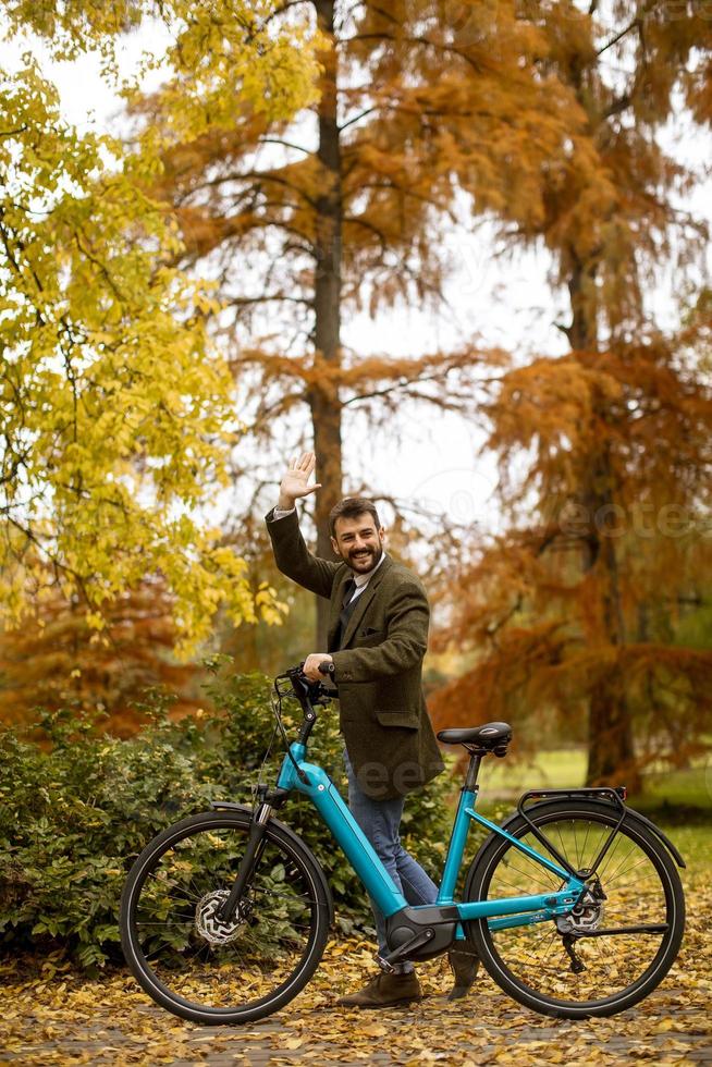 Apuesto joven con bicicleta eléctrica en el parque de otoño foto