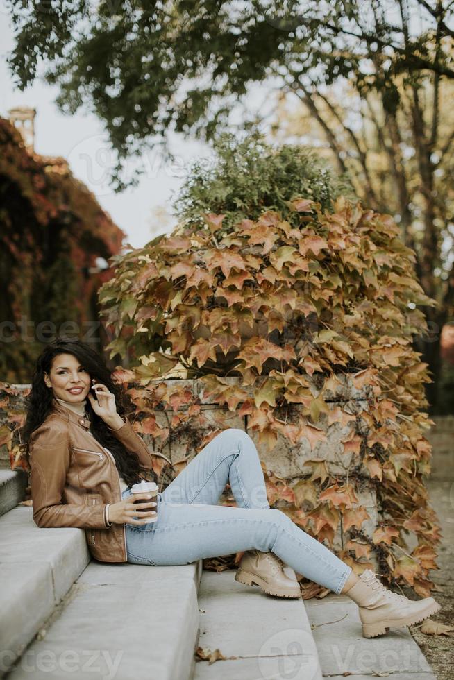 Mujer joven con teléfono móvil beber café para ir a las escaleras exteriores el día de otoño foto