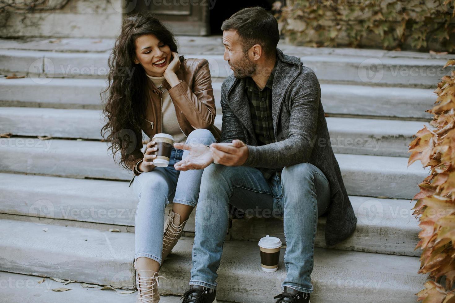 Young couple sitting on outdoor stairs on a autumn day and using mobile phone photo