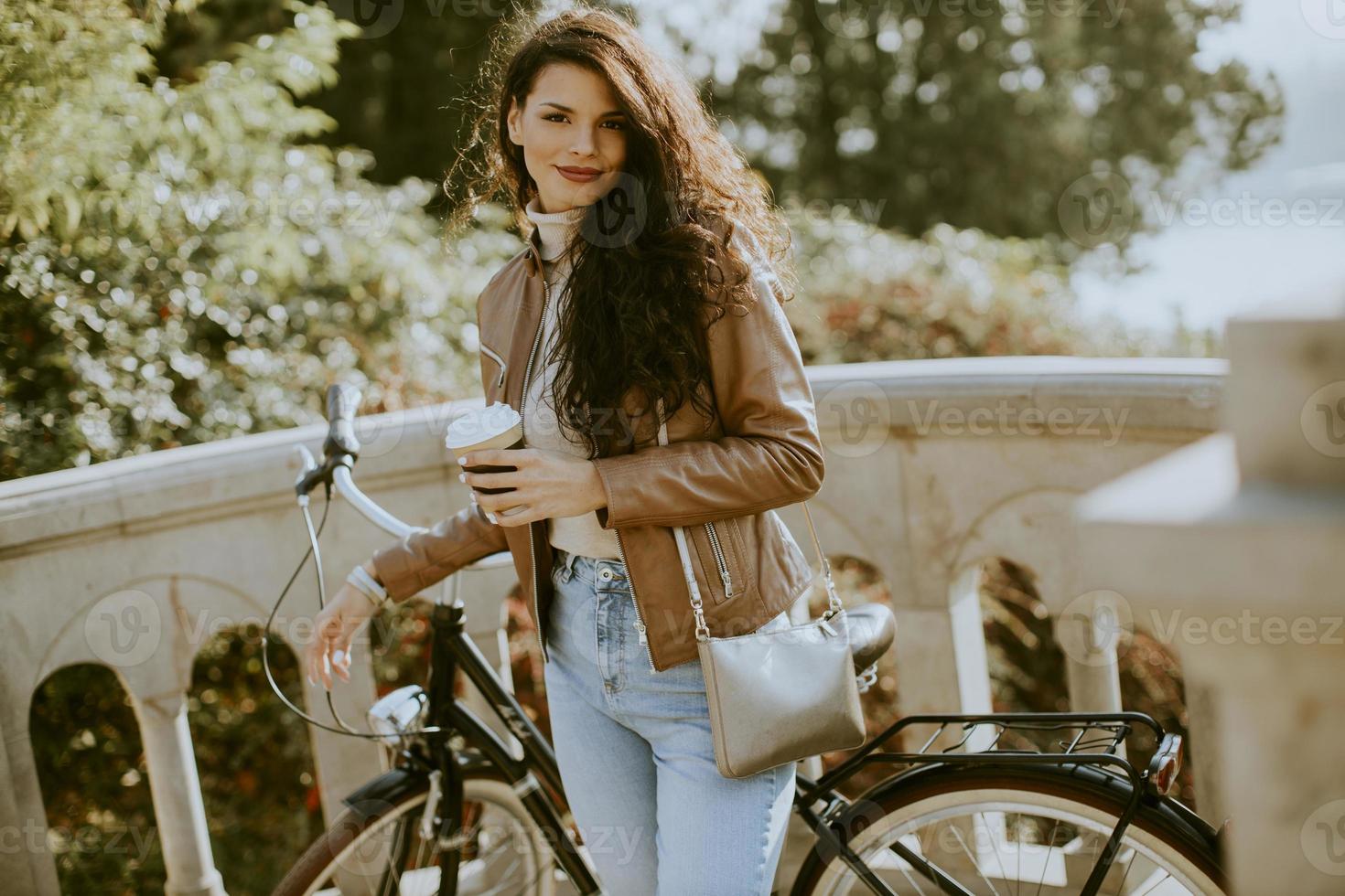 Mujer joven sosteniendo una taza de café para llevar en bicicleta en el día de otoño foto
