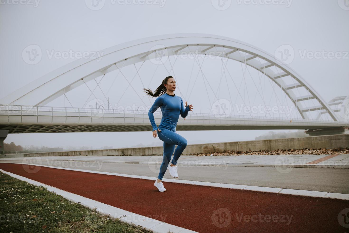 Mujer joven en traje azul corriendo por el río en la mañana de otoño foto