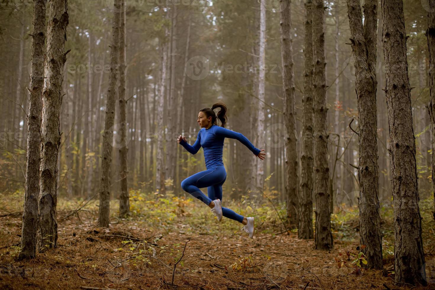 Mujer joven dando salto de altura en la pista forestal en otoño foto