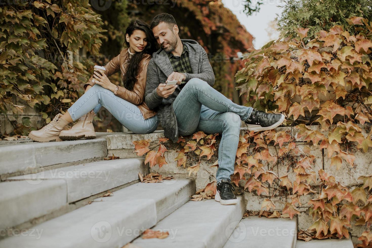 pareja joven sentada en las escaleras al aire libre en un día de otoño y usando un teléfono móvil foto