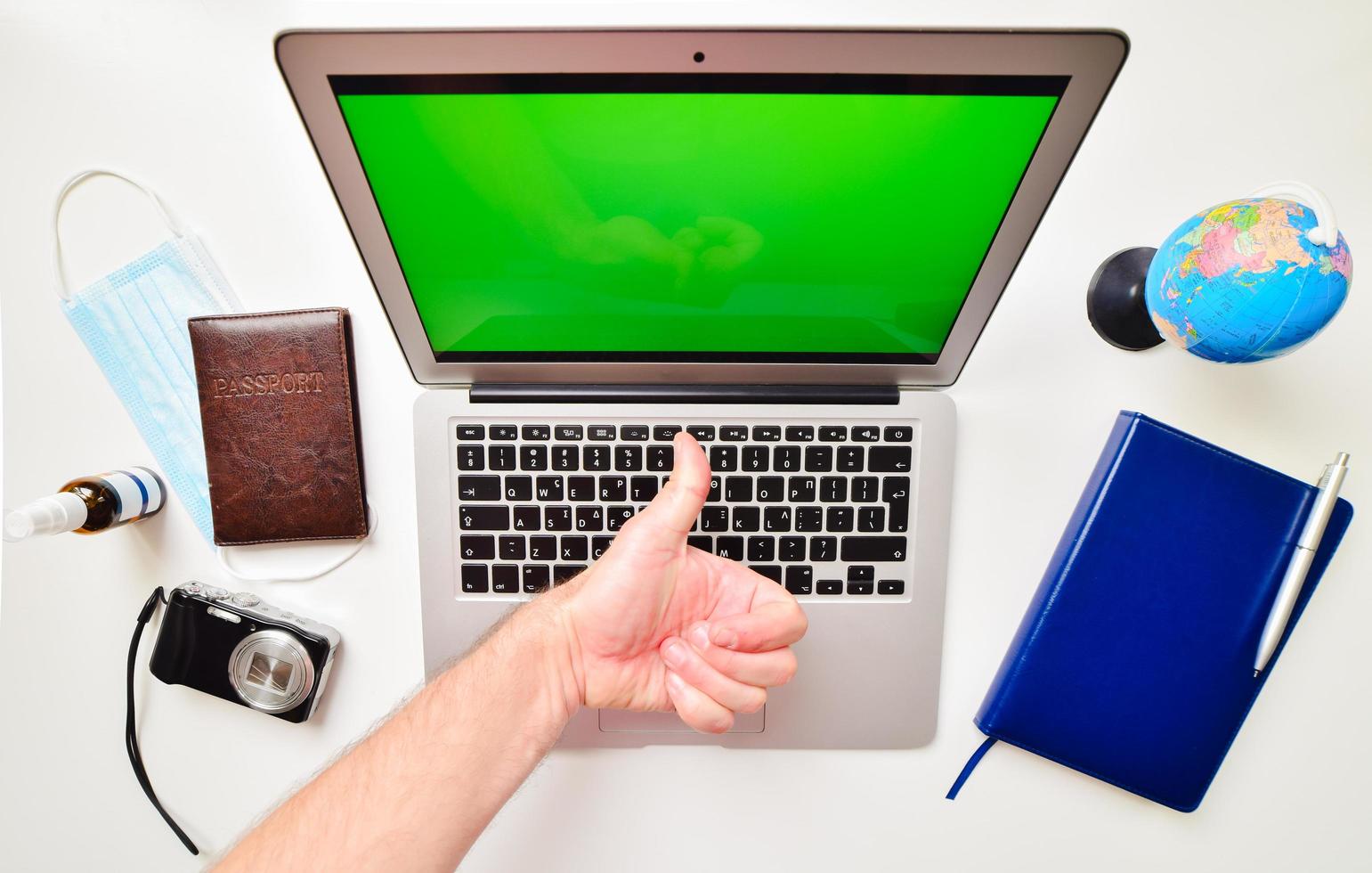 Desktop green screen computer with blue notebook, globe stand, passport, compact camera and hand show thumbs up on white background. Travel international reopening concept. photo