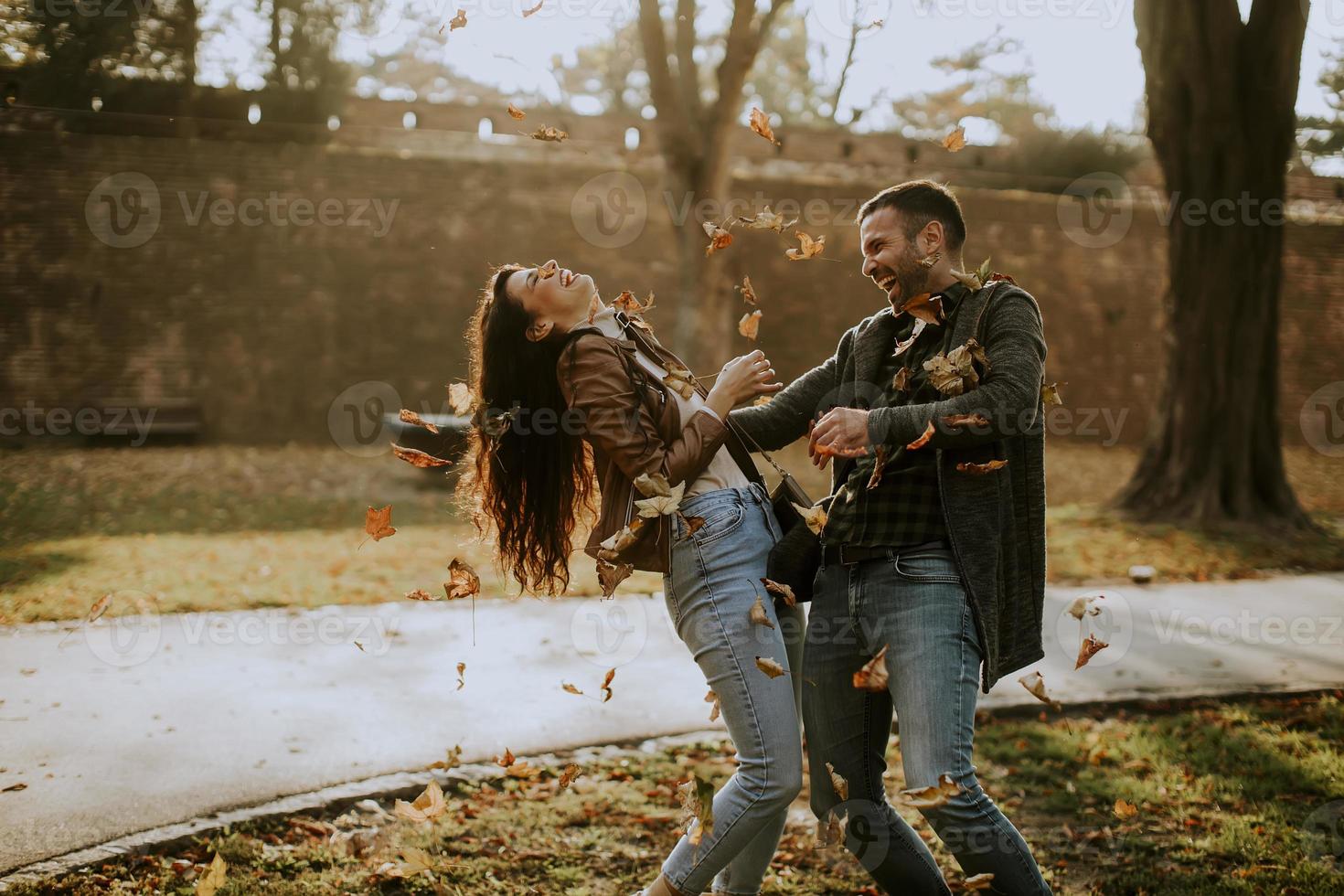 Young couple having fun with autumn leaves in the park photo