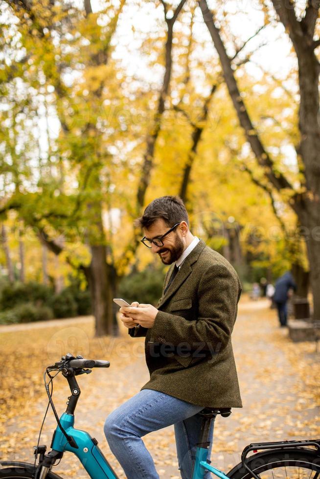 Joven con bicicleta eléctrica en el parque de otoño foto