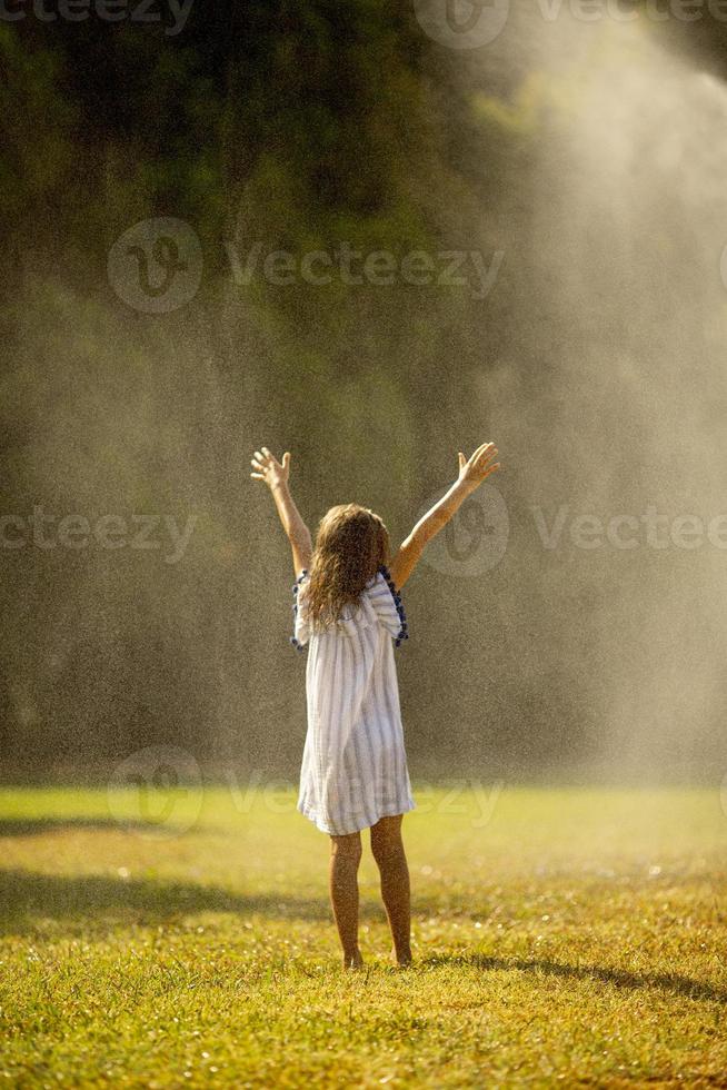 Cute little girl having fun under irrigation sprinkler photo