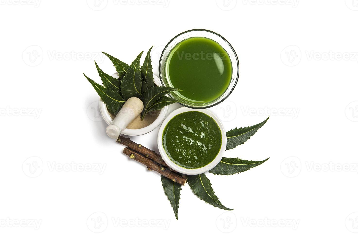 Medicinal Neem leaves in mortar and pestle with neem paste, juice and twigs on white background photo