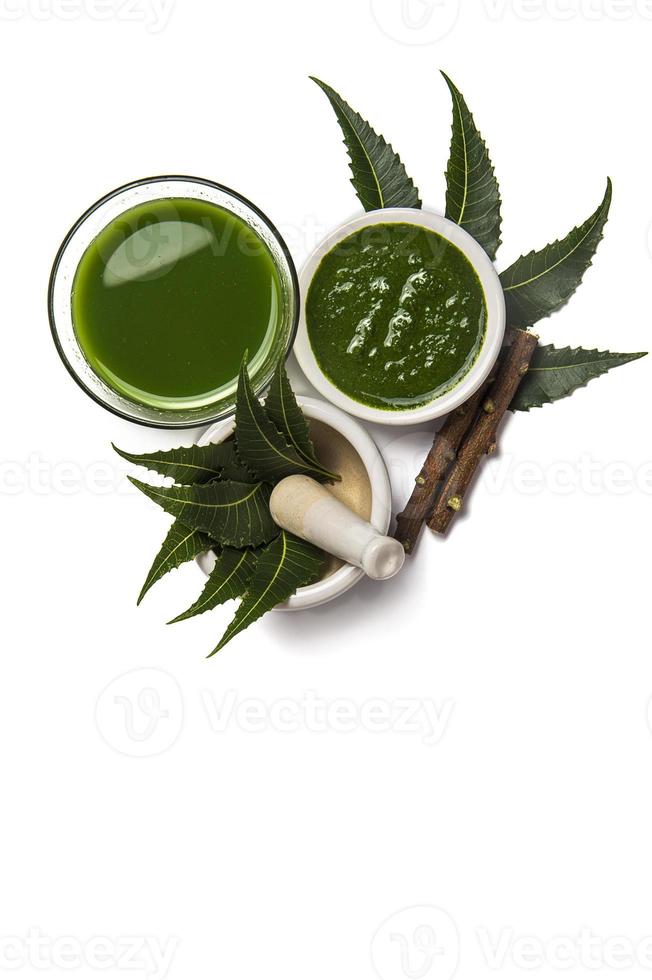 Medicinal Neem leaves in mortar and pestle with neem paste, juice and twigs on white background photo