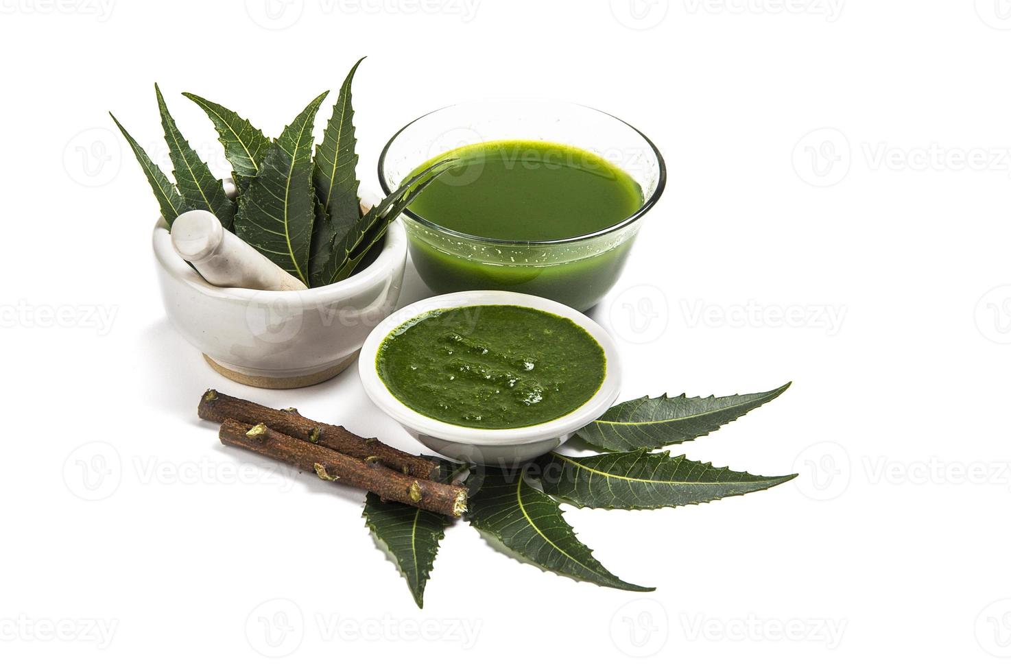 Medicinal Neem leaves in mortar and pestle with neem paste, juice and twigs on white background photo