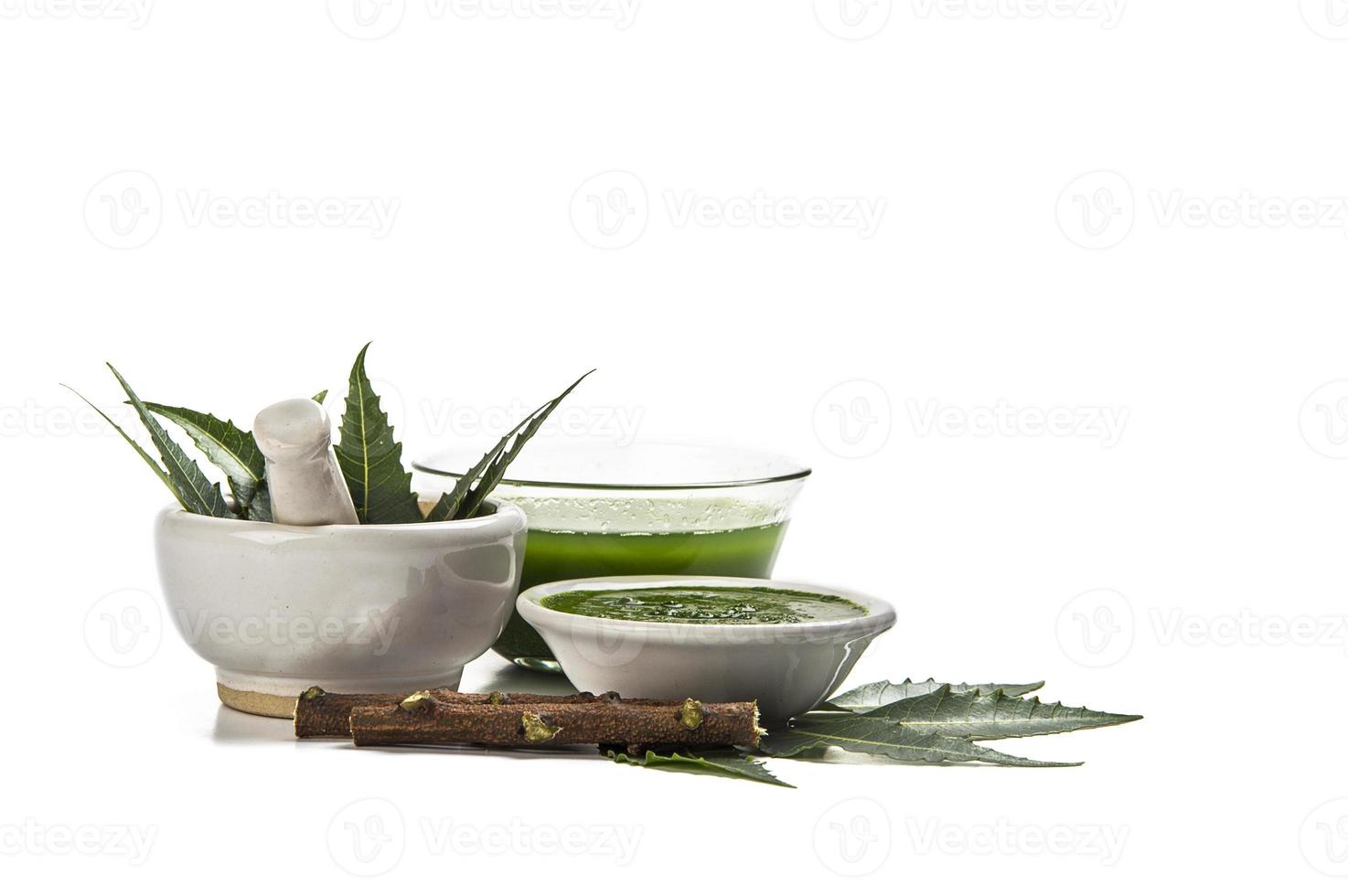 Medicinal Neem leaves in mortar and pestle with neem paste, juice and twigs on white background photo