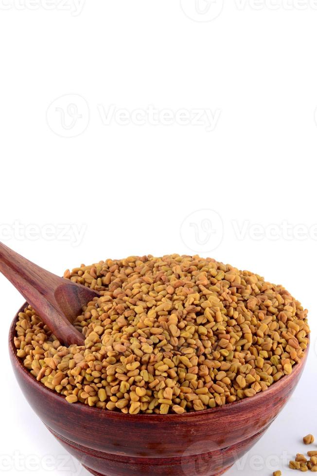 Fenugreek seeds in wooden bowl with spoon isolated on white background photo