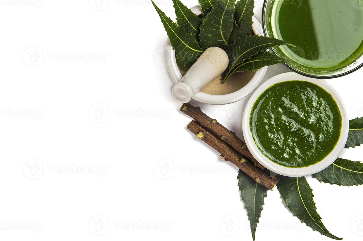 Medicinal Neem leaves in mortar and pestle with neem paste, juice and twigs on white background photo