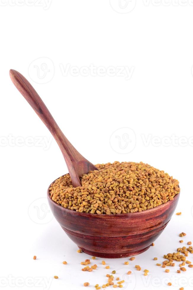 Fenugreek seeds in wooden bowl with spoon isolated on white background photo