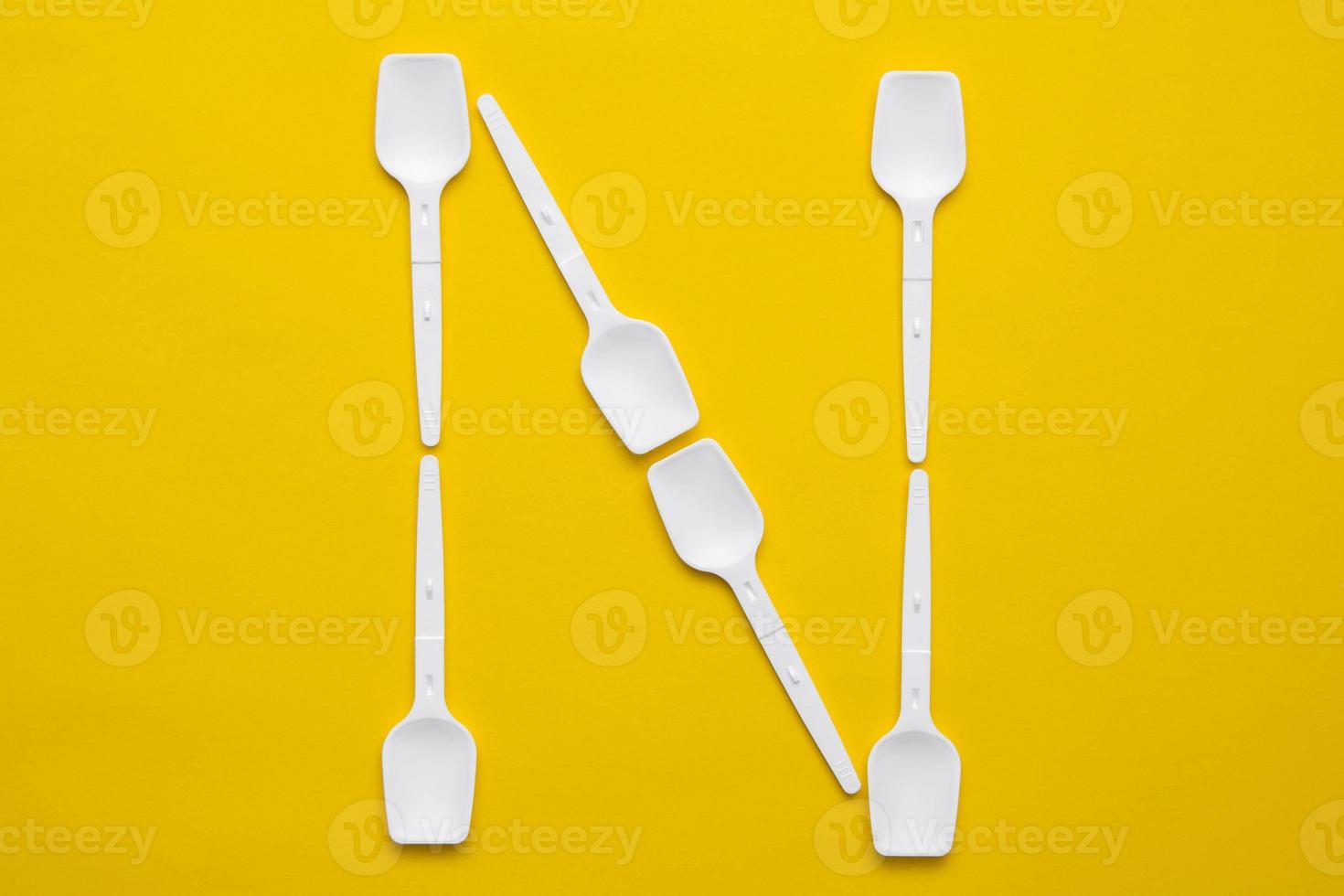 White plastic spoons in the form of letter N on yellow background. Top view. Copy, empty space for text photo