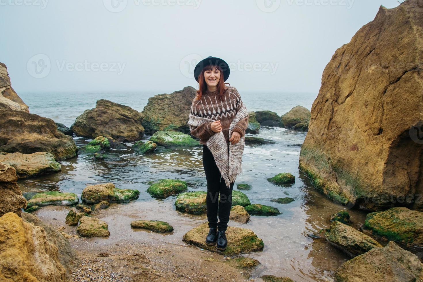 Woman in a hat and scarf standing on a rock against a beautiful sea on horizon photo