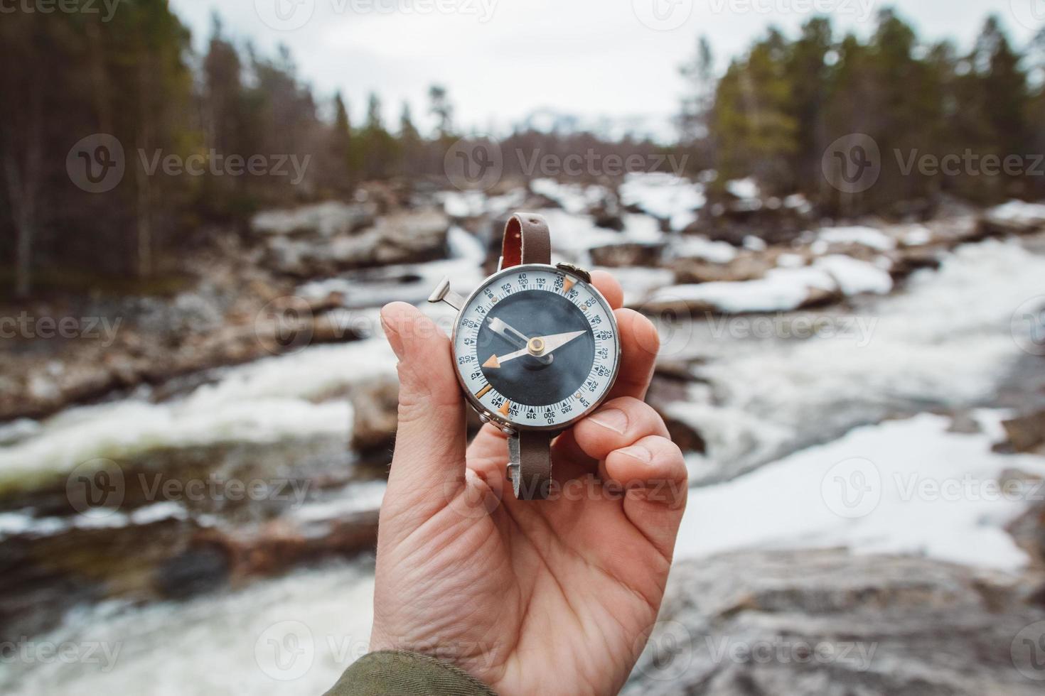 Beautiful male hand holds a magnetic compass against the background of mountain river, rocks and forest. The concept of finding yourself the way and the truth photo