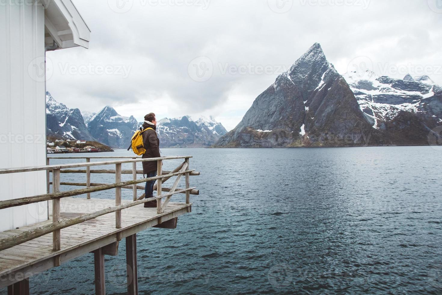 Hombre viajero con una mochila de pie sobre un muelle de madera el fondo de montañas nevadas y el lago. lugar para texto o publicidad foto