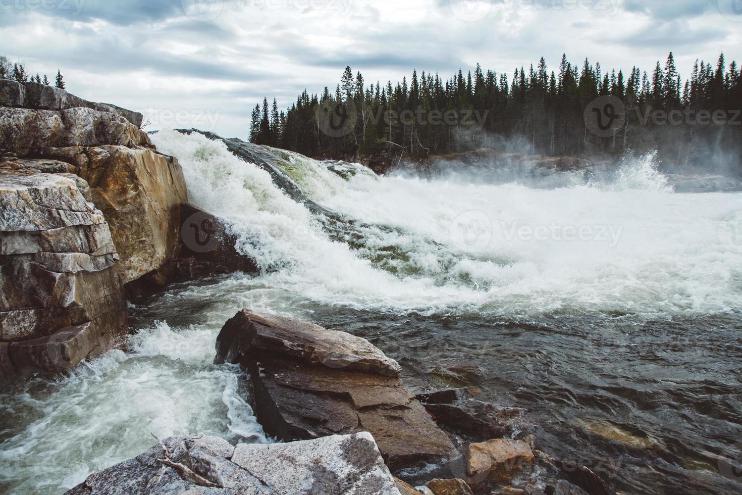 Waves and splashes of mountain river on background of forest and dramatic sky. Forest river water landscape. Wild river in mountain forrest panorama photo