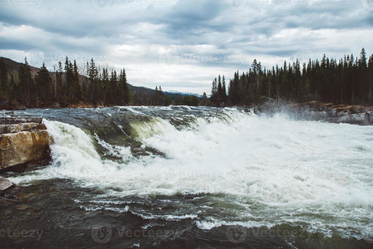 Waves and splashes of mountain river on background of forest and dramatic sky. Forest river water landscape. Wild river in mountain forrest panorama photo