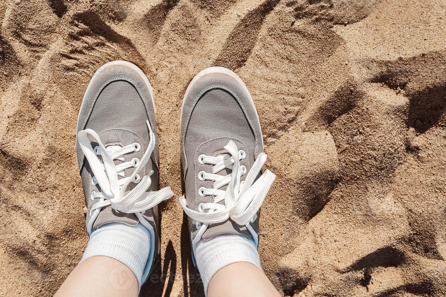 Legs in gray sneakers on beach sand. photo