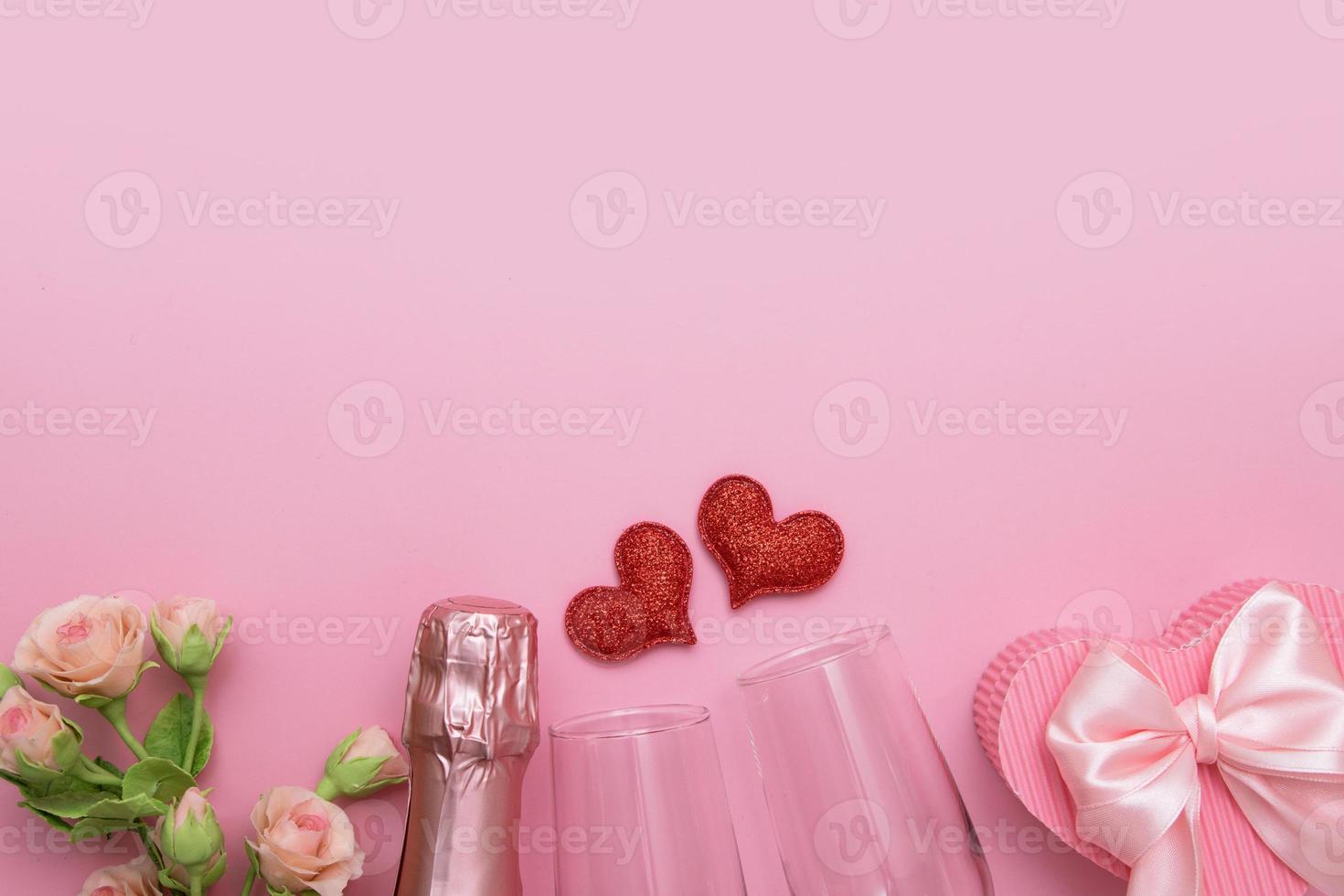 Top view two red hearts, glasses, champagne, flowers on a pink background with copy space valentines day date or party concept photo