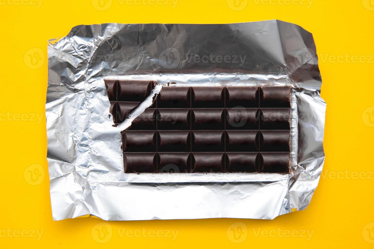 Bar of chocolate in silver foil on yellow background photo