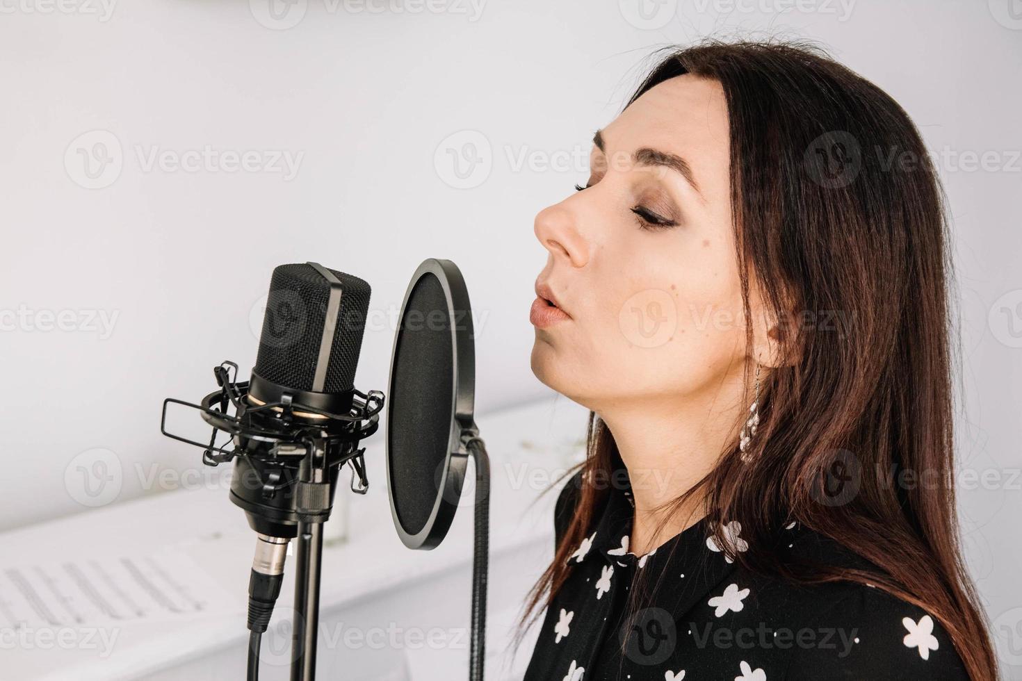 Portrait of beautiful woman sings a song near a microphone in a recording studio. Place for text or advertising photo
