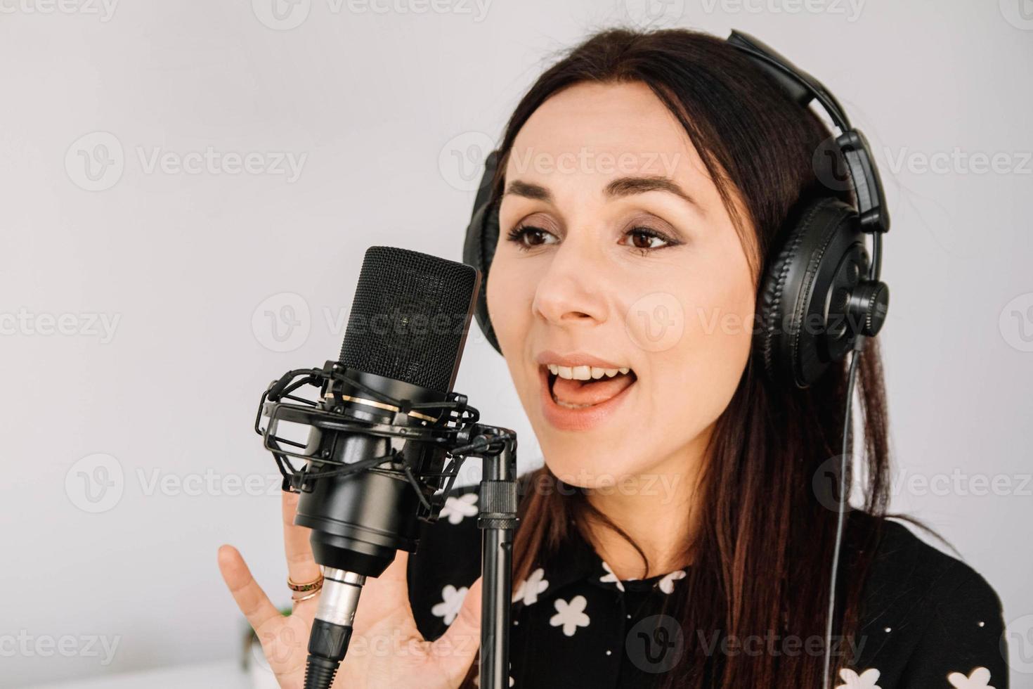 Beautiful woman in headphones sings a song near a microphone in a recording studio. Place for text or advertising photo