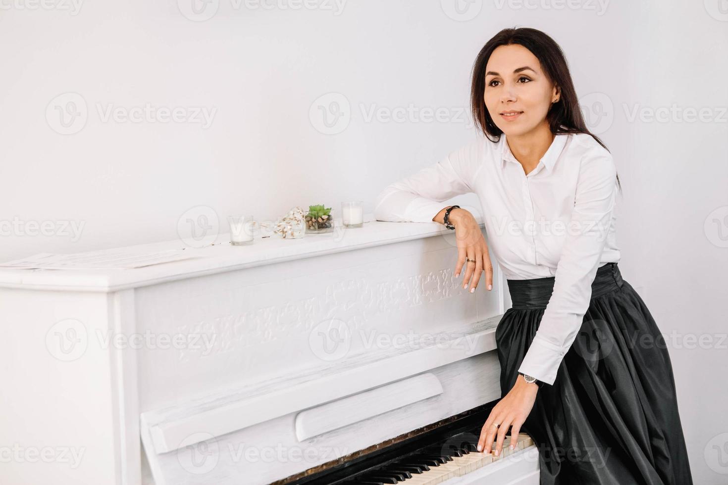 Beautiful woman dressed in white shirt playing on white piano. Place for text or advertising photo