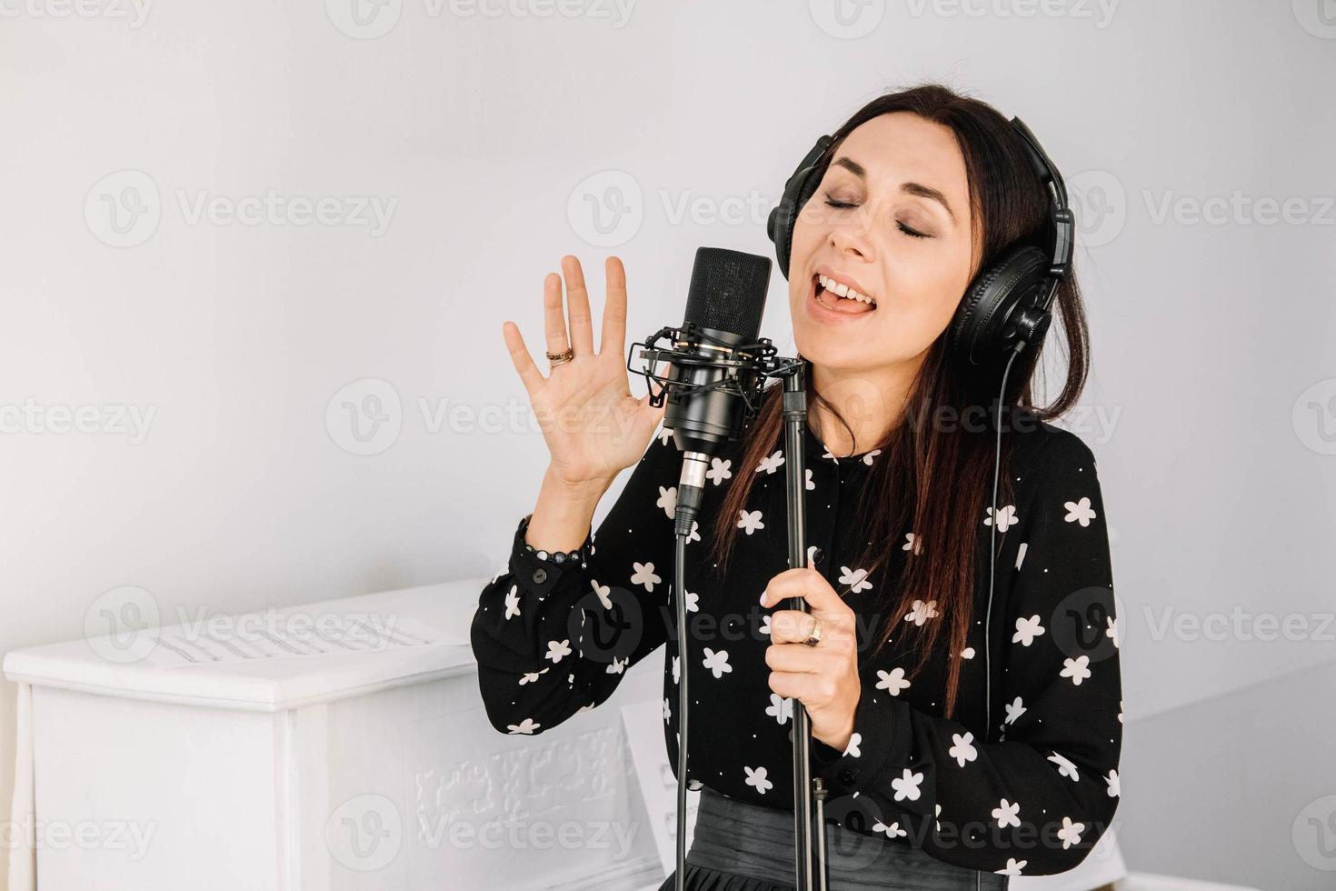 Beautiful woman in headphones sings a song near a microphone in a recording studio. Place for text or advertising photo