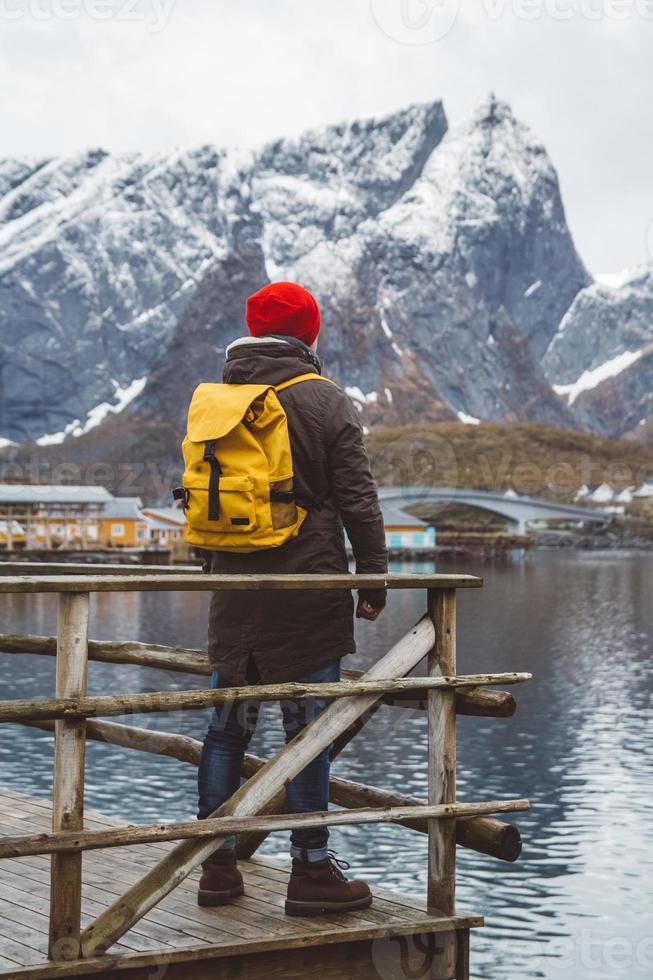 Young man with a backpack standing on a wooden pier the background of snowy mountains and lake. Place for text or advertising photo