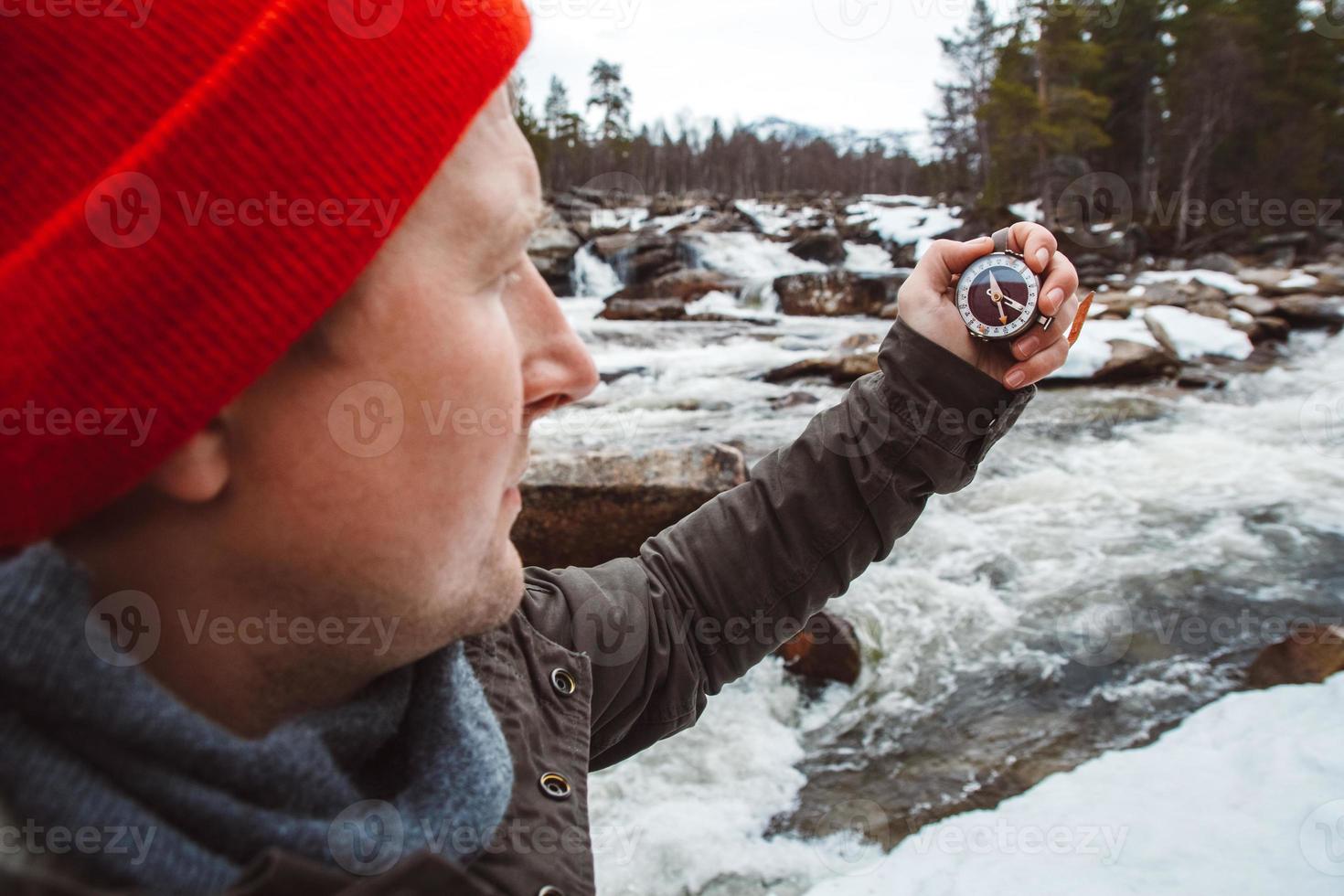 Traveler man holding compass on background of mountain river, rocks and forest. Shoot from the back. Place for text or advertising photo