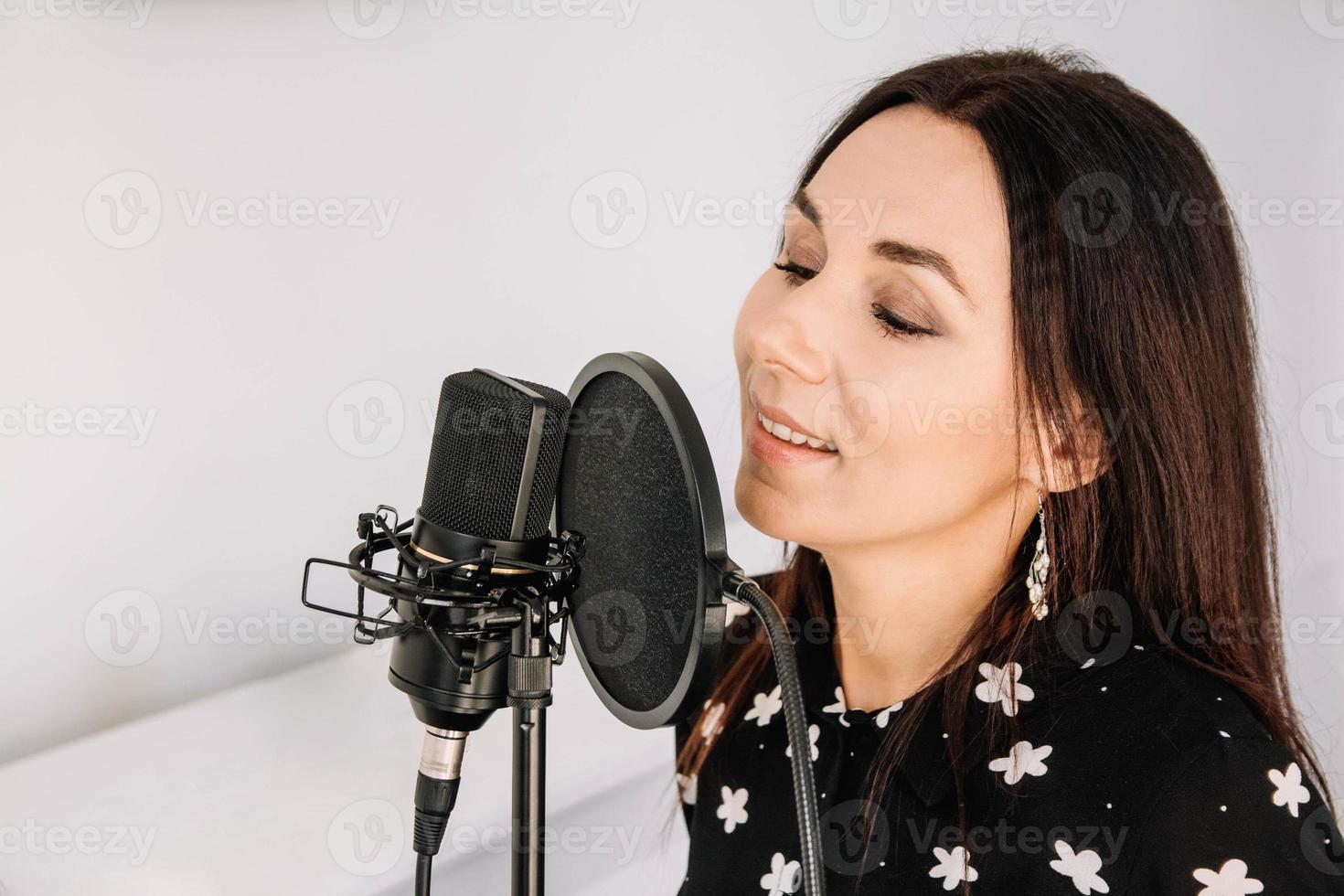 Portrait of beautiful woman sings a song near a microphone in a recording studio. Place for text or advertising photo