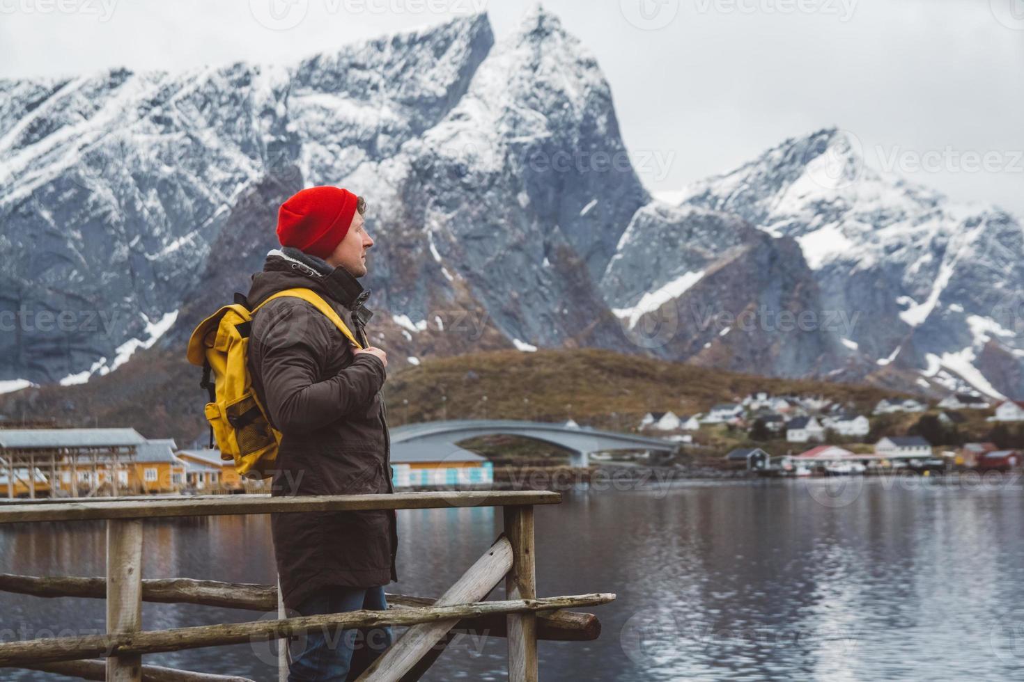 joven con una mochila de pie sobre un muelle de madera el fondo de montañas nevadas y el lago. lugar para texto o publicidad foto