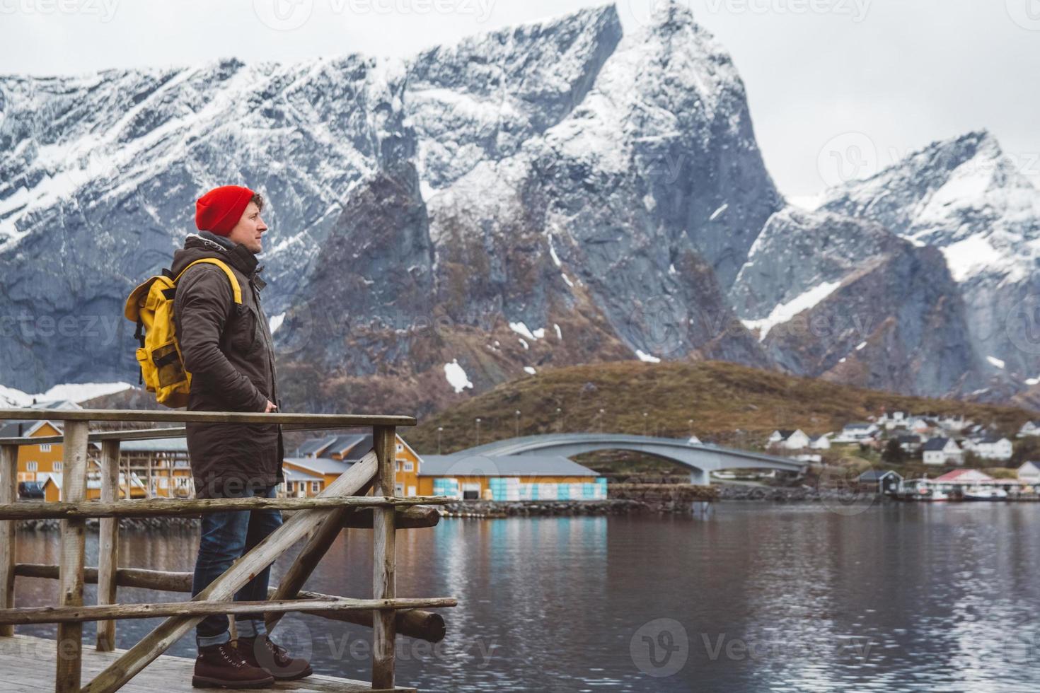 Young man with a backpack standing on a wooden pier the background of snowy mountains and lake. Place for text or advertising photo