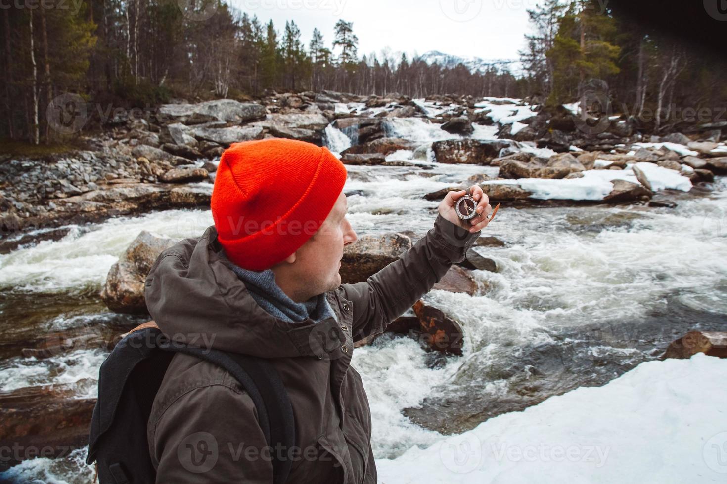 Traveler man holding compass on background of mountain river, rocks and forest. Shoot from the back. Place for text or advertising photo