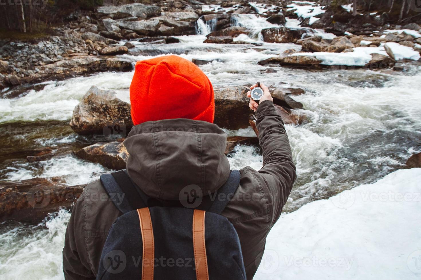 hombre viajero con brújula sobre fondo de río de montaña, rocas y bosque. disparar desde la espalda. lugar para texto o publicidad foto