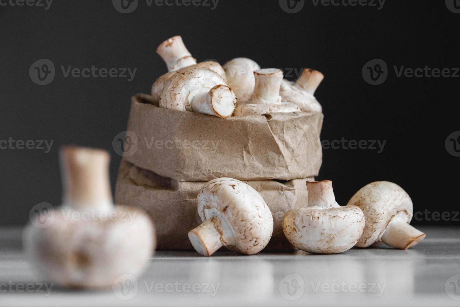 champiñones champiñones en una bolsa de papel sobre una mesa de madera blanca. lugar para texto o publicidad foto