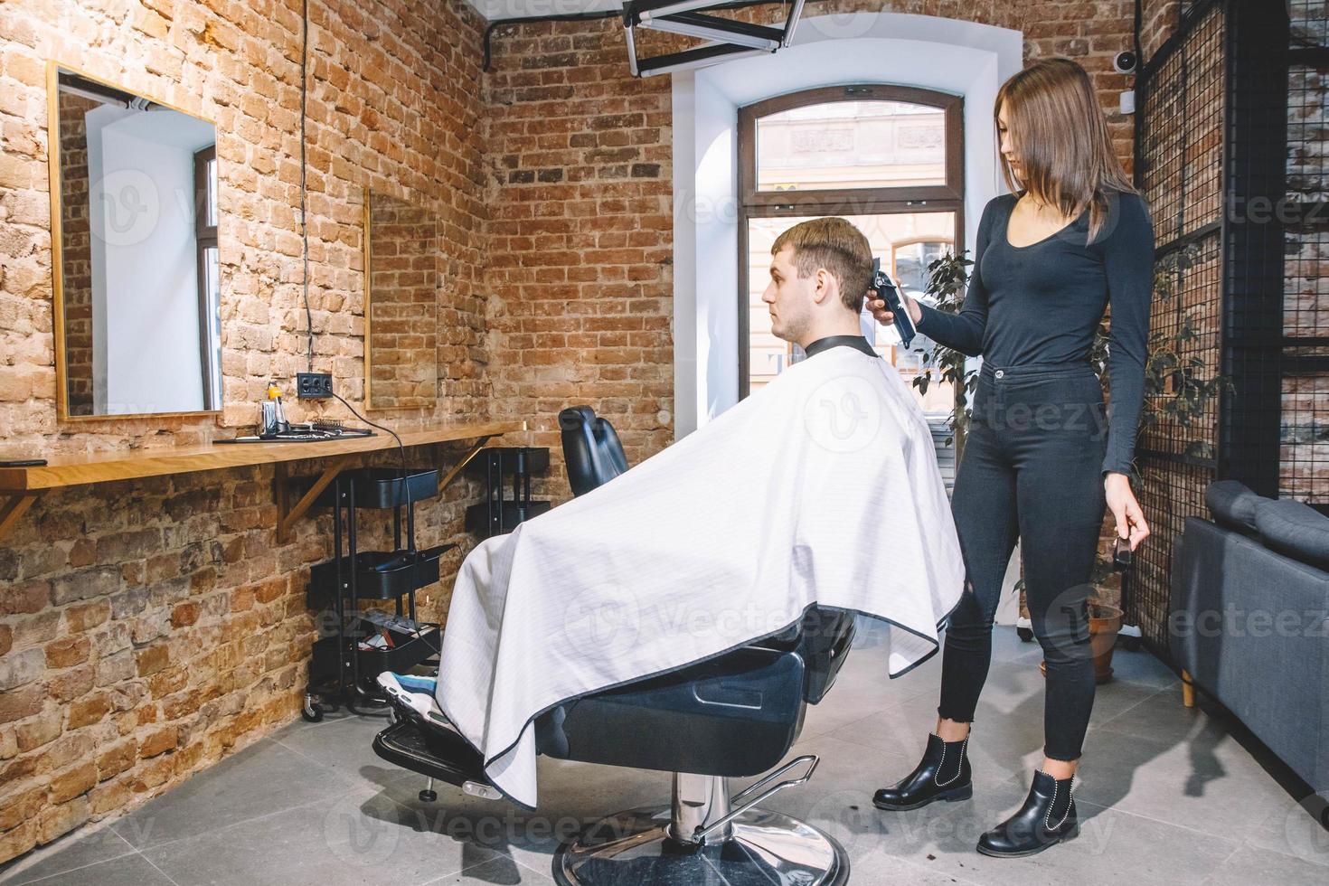 Peluquería mujer hace un corte de pelo la cabeza del cliente con una recortadora eléctrica en peluquería foto